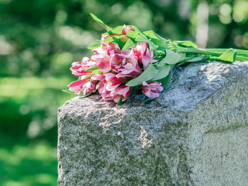 A bouquet of pink flowers sits atop a concrete grave marker at a cemetery.