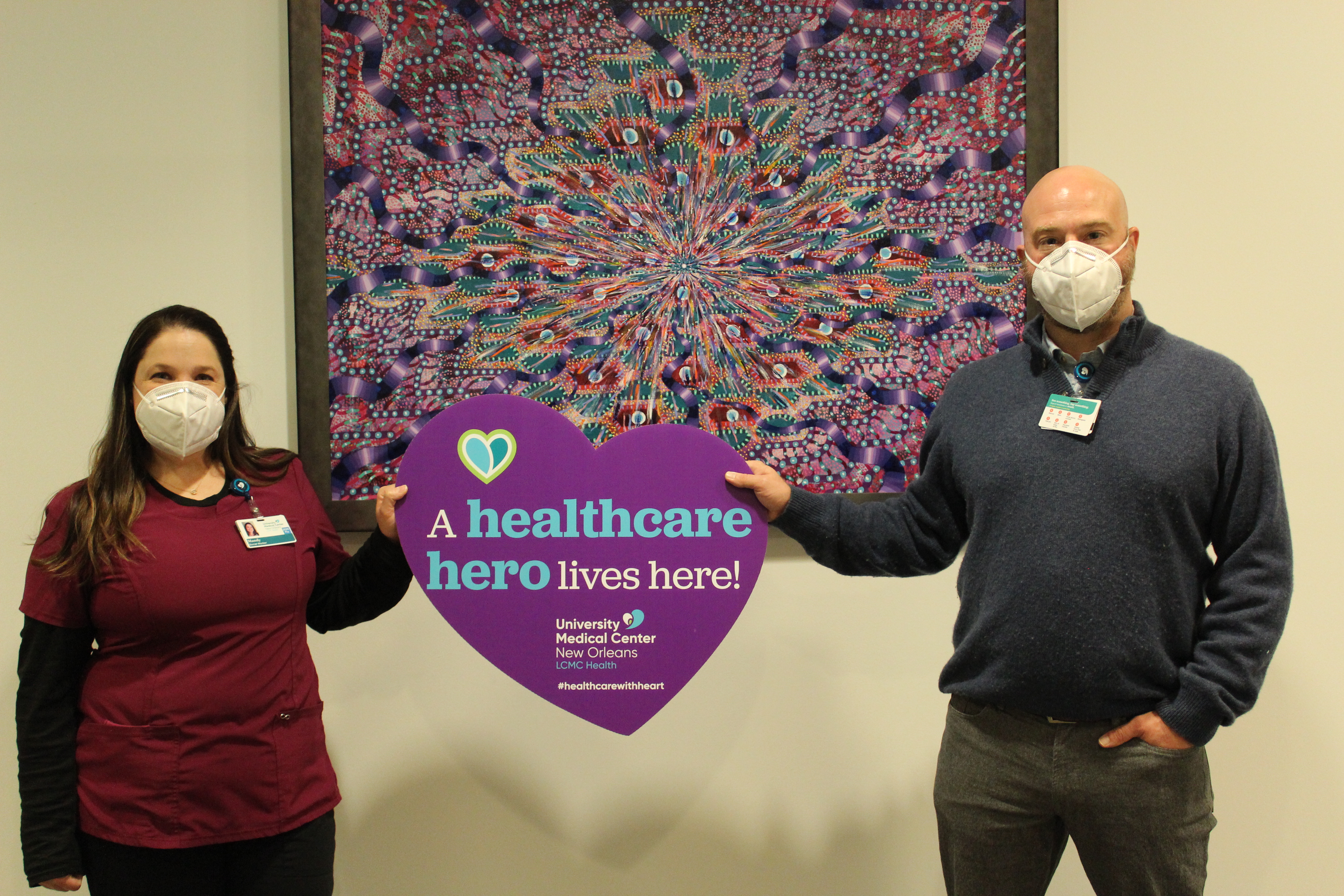 A woman and a man wearing face coverings hold a sign shaped like a purple heart that says "a healthcare hero lives here."
