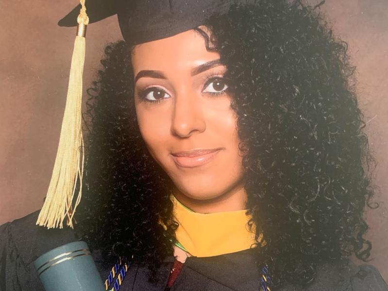 Nia Nicks poses with her Master's degree diploma tube in a cap and gown