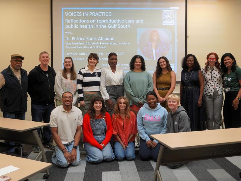 Diverse group of 15 people, some kneeling, posing in a Tulane School of Social Work classroom in front of a presentation on reproductive healthcare in the Gulf South.