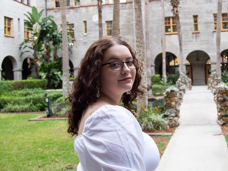 September Boyer, a Master of Social Work student at Tulane School of Social Work, smiles while standing in a stone courtyard with palm trees.