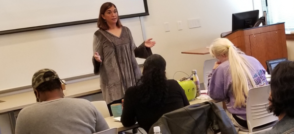 An adjunct professor gives a lecture in front of a class of students.