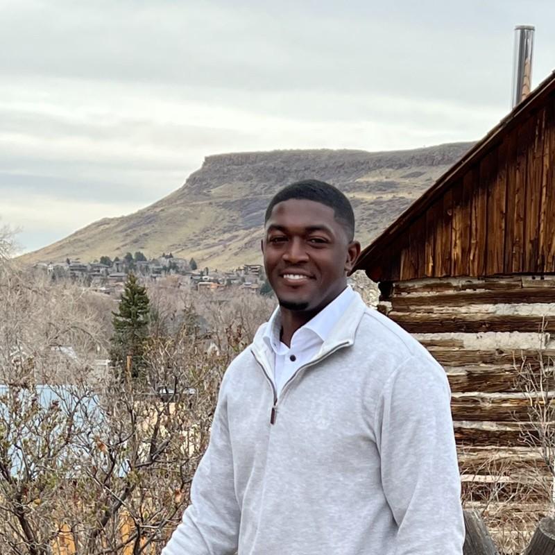 Nick Sanders smiles in front of a rustic background.