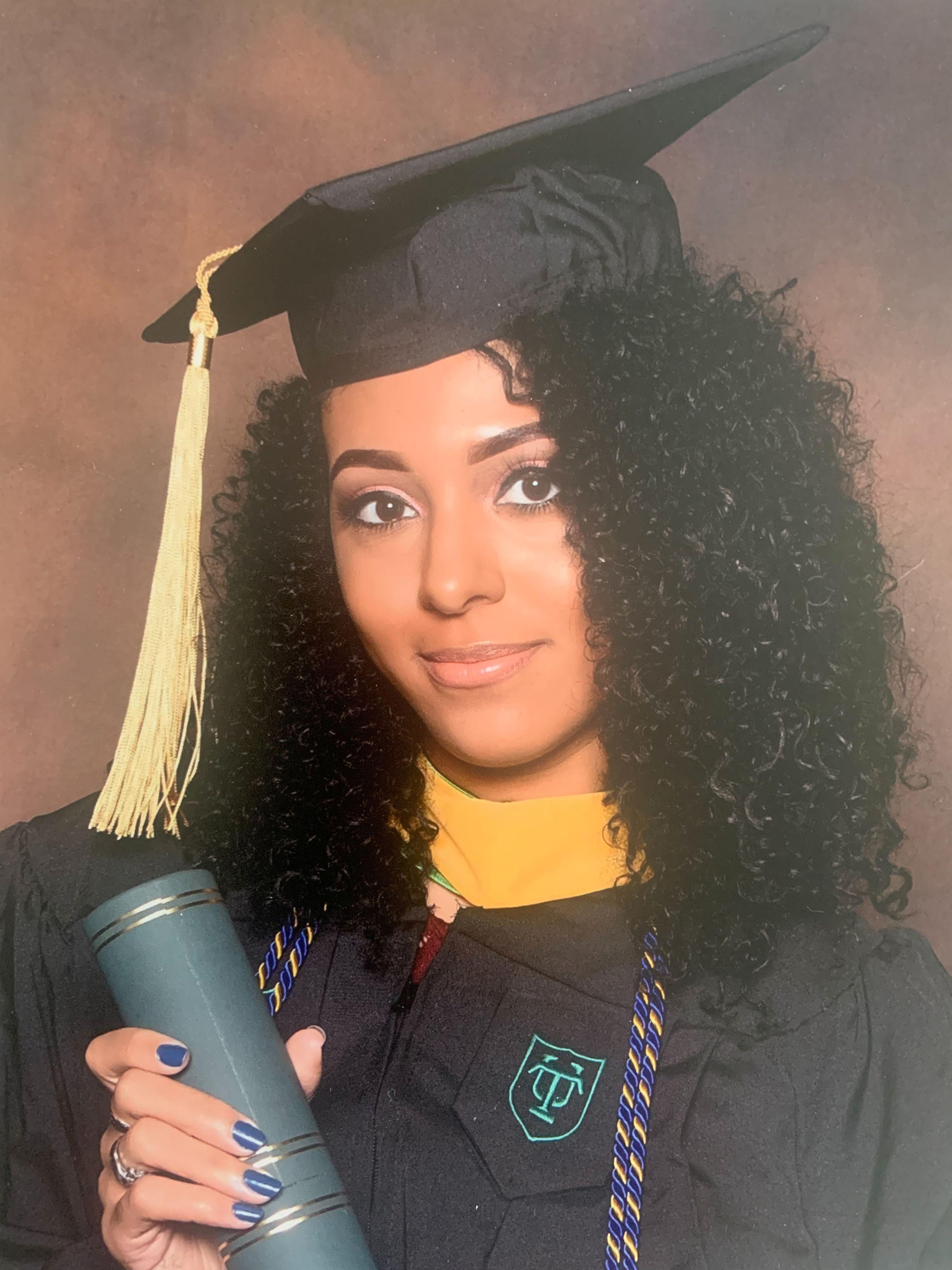 Nia Nicks poses with her Master's degree diploma tube in a cap and gown