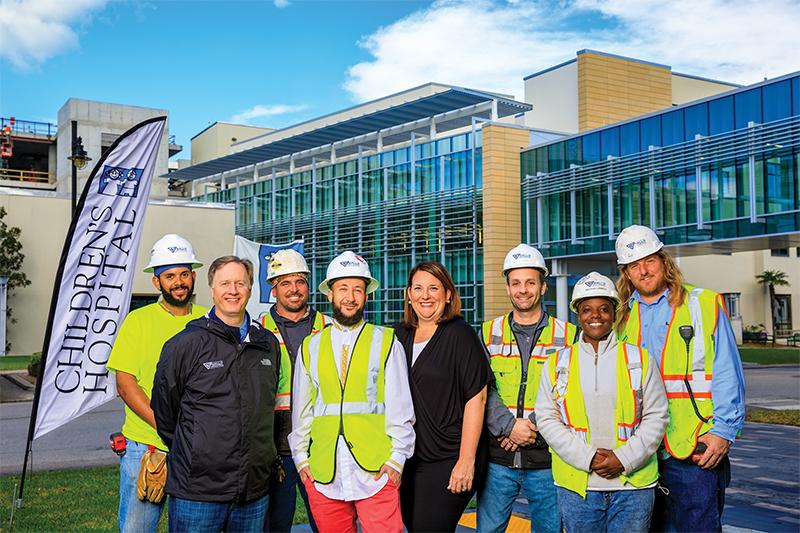 Powell DiGangi stands with a group of construction workers in front of a Children's Hospital.