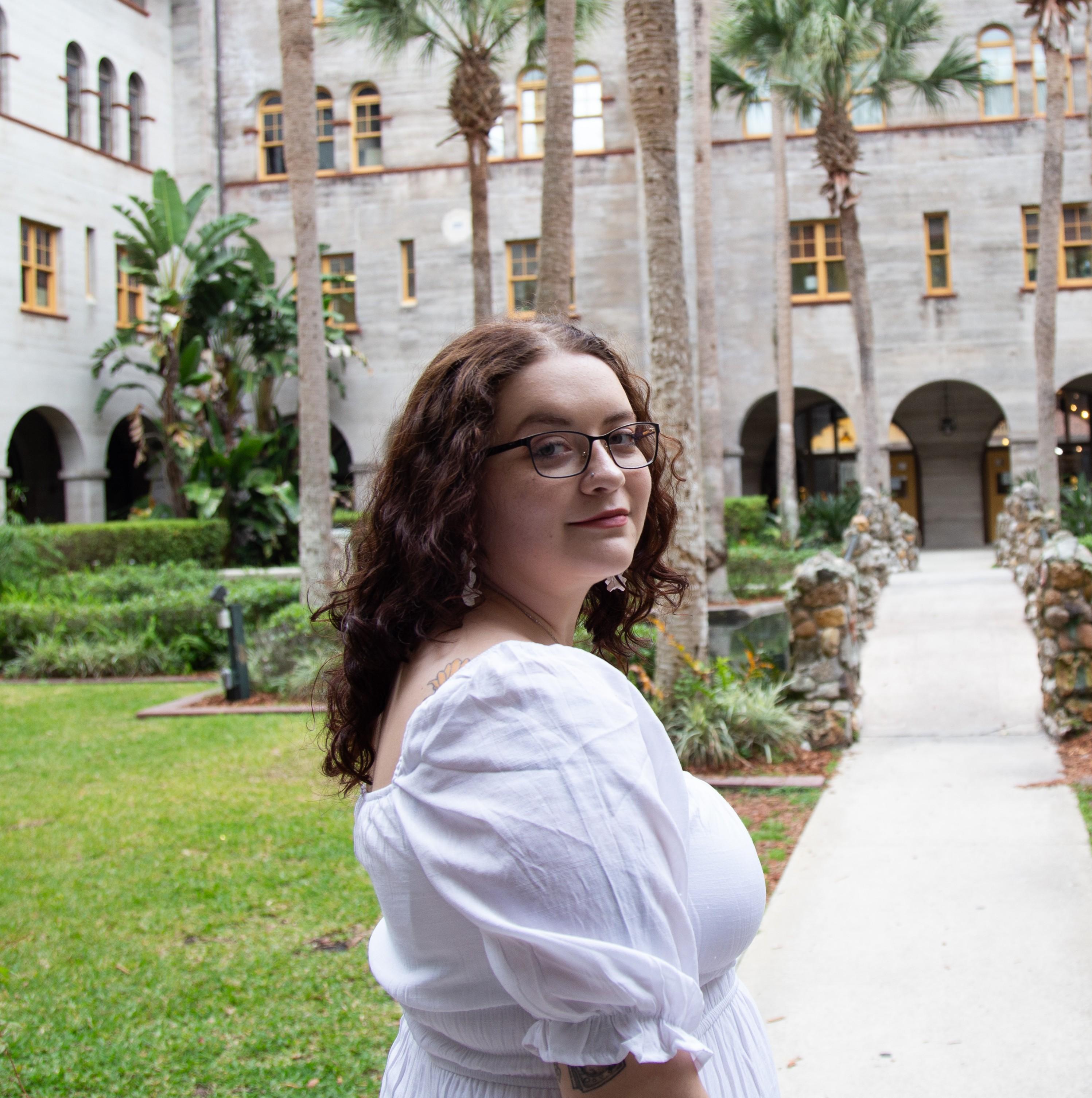 September Boyer, a Master of Social Work student at Tulane School of Social Work, smiles while standing in a stone courtyard with palm trees.