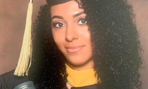 Nia Nicks poses with her Master's degree diploma tube in a cap and gown