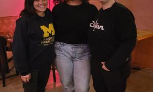 Three smiling people pose indoors with red lighting.